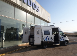 Furgoneta nueva, 
IVECO Camper,
Modelo  35S16A8V de 12m3,
Con cambio automático Hi Matic de 8 velocidades.  IVECO Daily Camper, una de las opciones más amplias del segmento con un espacio habitable de 12 metros cúbicos, con una longitud de 6 metros y una altura interior de 1,9 m. No obstante, estas dos últimas cifras pueden crecer hasta los 2,1 m de altura y 18 m3 de capacidad. Su carrocería presenta una amplia puerta corredera en el lateral derecho, escalón posterior y unas puertas traseras con apertura de 270º, sin olvidarnos de un habitáculo plano sin obstáculos. Su configuración polivalente permite que hasta 4 pasajeros viajen y pernocten en ella, con dos camas de matrimonio desmontables.  Toma como base la Daily destinada para uso profesional con mecánica diésel 2,3 litros Heavy Duty de 156 CV y 380 Nm de par motor, y cambio automático de 8 velocidades Hi Matic, destacando por ser una de las furgonetas con mayor maniobrabilidad del segmento.  Asimismo, cuenta con diversas ayudas sumamente interesantes para quienes no están acostumbrados a conducir este tipo de vehículos, como es por ejemplo el asistente de viento lateral.  Respecto a su interior, dice la marca que ha empleado materiales ligeros y duraderos basados principalmente en varios tipos de plásticos. Así pues, nos encontramos con un espacio capaz de albergar a cuatro huéspedes perfectamente equipado. La parte trasera se ha pensado de forma modular, pues cumple las funciones de dormitorio con una litera compuesta por dos camas de matrimonio de 198 x 130 cm con un baúl de almacenaje, comedor para esas cuatro personas, así como maletero con capacidad suficiente para guardar en él unas bicicletas o una pequeña motocicleta.  Dispone también de un baño completo con inodoro, lavabo y ducha, además de una cocina con dos fuegos, fregadero de un seno y nevera-congelador de 75 litros, estando todas las “estancias” perfectamente iluminadas gracias a las tres claraboyas y una iluminación interior 100 % LED. En cuanto al abastecimiento, corre a cargo de un depósito de 90 litros de aguas sucias y limpias y de una una placa solar de 160 W, siendo además capaz de suministrar corriente a 220 V con una potencia máxima de 1.500 W.  No obstante, para quienes prefieran tomar el aire fresco incluye un toldo de 3,7 metros y un foco LED bajo el cual poder colocar la mesa y sillas de camping. En el apartado multimedia cuenta con lo más esencial, como es una radio DAB, conexión USB y manos libres Bluetooth, aunque carece de la ya necesaria conectividad Android Auto y Apple CarPlay.