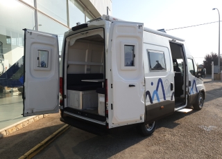 Furgoneta nueva, 
IVECO Camper,
Modelo  35S16A8V de 12m3,
Con cambio automático Hi Matic de 8 velocidades.  IVECO Daily Camper, una de las opciones más amplias del segmento con un espacio habitable de 12 metros cúbicos, con una longitud de 6 metros y una altura interior de 1,9 m. No obstante, estas dos últimas cifras pueden crecer hasta los 2,1 m de altura y 18 m3 de capacidad. Su carrocería presenta una amplia puerta corredera en el lateral derecho, escalón posterior y unas puertas traseras con apertura de 270º, sin olvidarnos de un habitáculo plano sin obstáculos. Su configuración polivalente permite que hasta 4 pasajeros viajen y pernocten en ella, con dos camas de matrimonio desmontables.  Toma como base la Daily destinada para uso profesional con mecánica diésel 2,3 litros Heavy Duty de 156 CV y 380 Nm de par motor, y cambio automático de 8 velocidades Hi Matic, destacando por ser una de las furgonetas con mayor maniobrabilidad del segmento.  Asimismo, cuenta con diversas ayudas sumamente interesantes para quienes no están acostumbrados a conducir este tipo de vehículos, como es por ejemplo el asistente de viento lateral.  Respecto a su interior, dice la marca que ha empleado materiales ligeros y duraderos basados principalmente en varios tipos de plásticos. Así pues, nos encontramos con un espacio capaz de albergar a cuatro huéspedes perfectamente equipado. La parte trasera se ha pensado de forma modular, pues cumple las funciones de dormitorio con una litera compuesta por dos camas de matrimonio de 198 x 130 cm con un baúl de almacenaje, comedor para esas cuatro personas, así como maletero con capacidad suficiente para guardar en él unas bicicletas o una pequeña motocicleta.  Dispone también de un baño completo con inodoro, lavabo y ducha, además de una cocina con dos fuegos, fregadero de un seno y nevera-congelador de 75 litros, estando todas las “estancias” perfectamente iluminadas gracias a las tres claraboyas y una iluminación interior 100 % LED. En cuanto al abastecimiento, corre a cargo de un depósito de 90 litros de aguas sucias y limpias y de una una placa solar de 160 W, siendo además capaz de suministrar corriente a 220 V con una potencia máxima de 1.500 W.  No obstante, para quienes prefieran tomar el aire fresco incluye un toldo de 3,7 metros y un foco LED bajo el cual poder colocar la mesa y sillas de camping. En el apartado multimedia cuenta con lo más esencial, como es una radio DAB, conexión USB y manos libres Bluetooth, aunque carece de la ya necesaria conectividad Android Auto y Apple CarPlay.