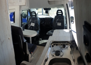 Furgoneta nueva, 
IVECO Camper,
Modelo  35S16A8V de 12m3,
Con cambio automático Hi Matic de 8 velocidades.  IVECO Daily Camper, una de las opciones más amplias del segmento con un espacio habitable de 12 metros cúbicos, con una longitud de 6 metros y una altura interior de 1,9 m. No obstante, estas dos últimas cifras pueden crecer hasta los 2,1 m de altura y 18 m3 de capacidad. Su carrocería presenta una amplia puerta corredera en el lateral derecho, escalón posterior y unas puertas traseras con apertura de 270º, sin olvidarnos de un habitáculo plano sin obstáculos. Su configuración polivalente permite que hasta 4 pasajeros viajen y pernocten en ella, con dos camas de matrimonio desmontables.  Toma como base la Daily destinada para uso profesional con mecánica diésel 2,3 litros Heavy Duty de 156 CV y 380 Nm de par motor, y cambio automático de 8 velocidades Hi Matic, destacando por ser una de las furgonetas con mayor maniobrabilidad del segmento.  Asimismo, cuenta con diversas ayudas sumamente interesantes para quienes no están acostumbrados a conducir este tipo de vehículos, como es por ejemplo el asistente de viento lateral.  Respecto a su interior, dice la marca que ha empleado materiales ligeros y duraderos basados principalmente en varios tipos de plásticos. Así pues, nos encontramos con un espacio capaz de albergar a cuatro huéspedes perfectamente equipado. La parte trasera se ha pensado de forma modular, pues cumple las funciones de dormitorio con una litera compuesta por dos camas de matrimonio de 198 x 130 cm con un baúl de almacenaje, comedor para esas cuatro personas, así como maletero con capacidad suficiente para guardar en él unas bicicletas o una pequeña motocicleta.  Dispone también de un baño completo con inodoro, lavabo y ducha, además de una cocina con dos fuegos, fregadero de un seno y nevera-congelador de 75 litros, estando todas las “estancias” perfectamente iluminadas gracias a las tres claraboyas y una iluminación interior 100 % LED. En cuanto al abastecimiento, corre a cargo de un depósito de 90 litros de aguas sucias y limpias y de una una placa solar de 160 W, siendo además capaz de suministrar corriente a 220 V con una potencia máxima de 1.500 W.  No obstante, para quienes prefieran tomar el aire fresco incluye un toldo de 3,7 metros y un foco LED bajo el cual poder colocar la mesa y sillas de camping. En el apartado multimedia cuenta con lo más esencial, como es una radio DAB, conexión USB y manos libres Bluetooth, aunque carece de la ya necesaria conectividad Android Auto y Apple CarPlay.