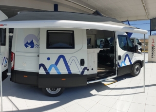 Furgoneta nueva, 
IVECO Camper,
Modelo  35S16A8V de 12m3,
Con cambio automático Hi Matic de 8 velocidades.  IVECO Daily Camper, una de las opciones más amplias del segmento con un espacio habitable de 12 metros cúbicos, con una longitud de 6 metros y una altura interior de 1,9 m. No obstante, estas dos últimas cifras pueden crecer hasta los 2,1 m de altura y 18 m3 de capacidad. Su carrocería presenta una amplia puerta corredera en el lateral derecho, escalón posterior y unas puertas traseras con apertura de 270º, sin olvidarnos de un habitáculo plano sin obstáculos. Su configuración polivalente permite que hasta 4 pasajeros viajen y pernocten en ella, con dos camas de matrimonio desmontables.  Toma como base la Daily destinada para uso profesional con mecánica diésel 2,3 litros Heavy Duty de 156 CV y 380 Nm de par motor, y cambio automático de 8 velocidades Hi Matic, destacando por ser una de las furgonetas con mayor maniobrabilidad del segmento.  Asimismo, cuenta con diversas ayudas sumamente interesantes para quienes no están acostumbrados a conducir este tipo de vehículos, como es por ejemplo el asistente de viento lateral.  Respecto a su interior, dice la marca que ha empleado materiales ligeros y duraderos basados principalmente en varios tipos de plásticos. Así pues, nos encontramos con un espacio capaz de albergar a cuatro huéspedes perfectamente equipado. La parte trasera se ha pensado de forma modular, pues cumple las funciones de dormitorio con una litera compuesta por dos camas de matrimonio de 198 x 130 cm con un baúl de almacenaje, comedor para esas cuatro personas, así como maletero con capacidad suficiente para guardar en él unas bicicletas o una pequeña motocicleta.  Dispone también de un baño completo con inodoro, lavabo y ducha, además de una cocina con dos fuegos, fregadero de un seno y nevera-congelador de 75 litros, estando todas las “estancias” perfectamente iluminadas gracias a las tres claraboyas y una iluminación interior 100 % LED. En cuanto al abastecimiento, corre a cargo de un depósito de 90 litros de aguas sucias y limpias y de una una placa solar de 160 W, siendo además capaz de suministrar corriente a 220 V con una potencia máxima de 1.500 W.  No obstante, para quienes prefieran tomar el aire fresco incluye un toldo de 3,7 metros y un foco LED bajo el cual poder colocar la mesa y sillas de camping. En el apartado multimedia cuenta con lo más esencial, como es una radio DAB, conexión USB y manos libres Bluetooth, aunque carece de la ya necesaria conectividad Android Auto y Apple CarPlay.